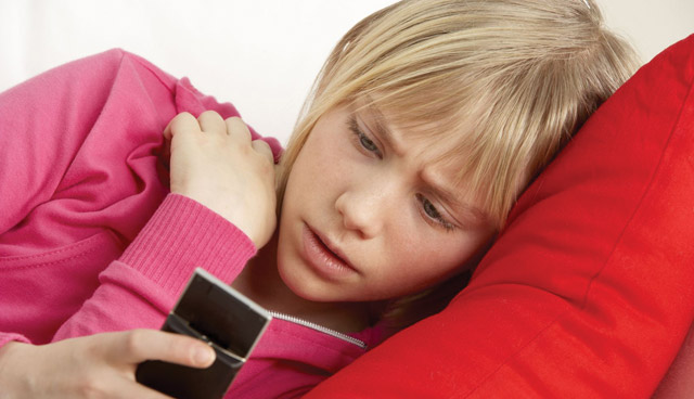 A teenager looking troubled while staring at their mobile phone