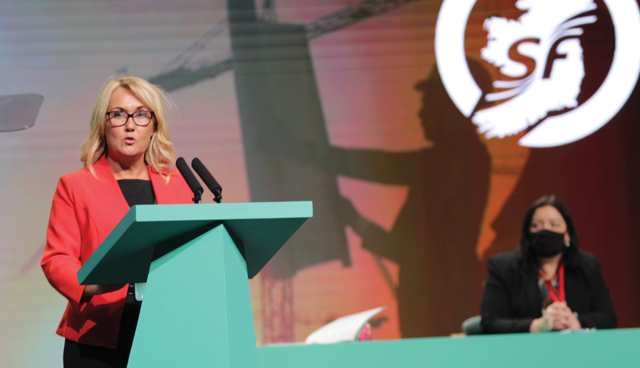 Ciara Ferguson MLA standing at a podium with Sinn Féin President Mary-Lou McDonald seated behind her